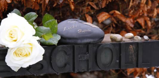 Weiße Rose und Steine auf dem Grabkreuz von Sophie Scholl