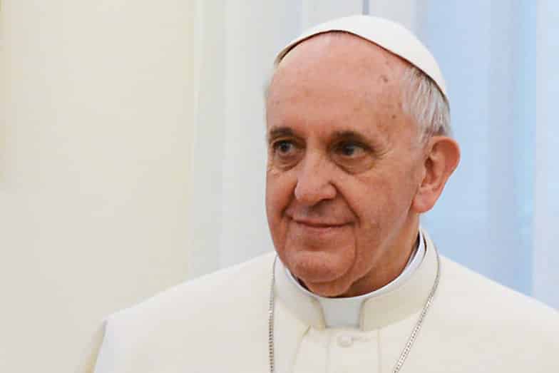 Papst Franziskus steht vor einem weißen Hintergrund.