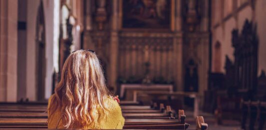 Eine Frau sitzt einsam in einer Kirche.