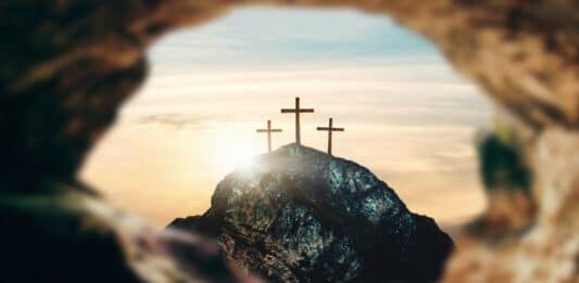 Ein Blick aus einem leeren Felsengrab auf drei Kreuz, die auf einem Hügel stehen.