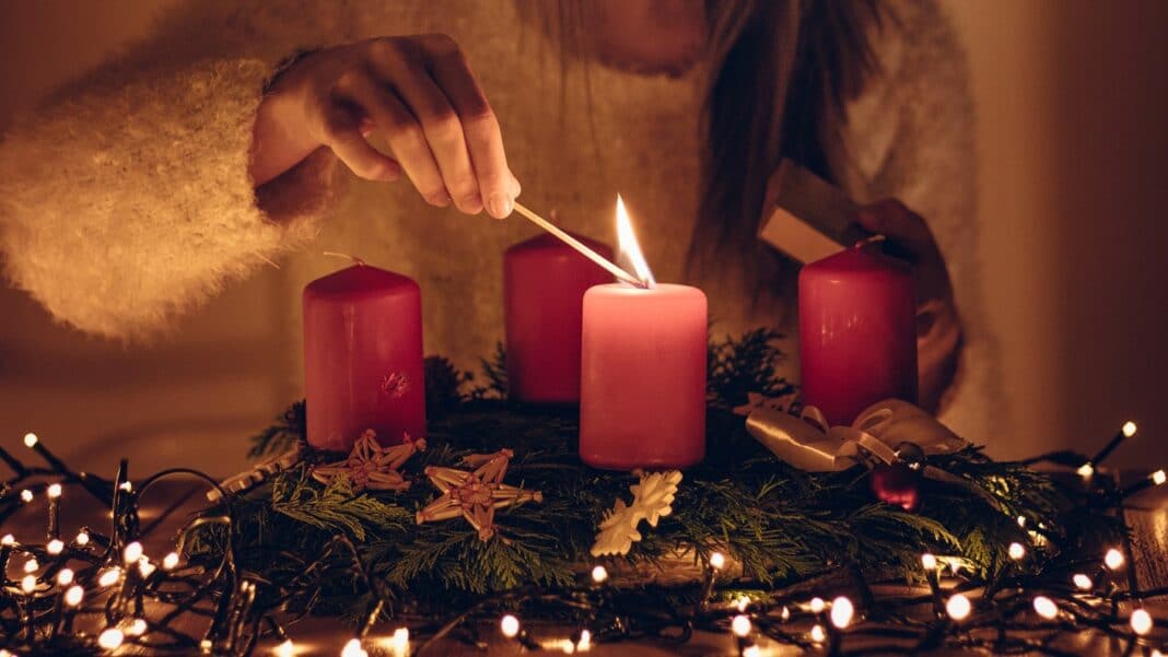 Eine junge Frau entzündet mit einem Streichholz die erste Kerze auf einem Adventskranz.