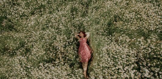 Ein Frau mit rotem Kleid liegt in einer weißen Blumenwiese.