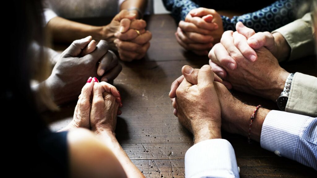 Ein Gruppe von Menschen sitzt im Kreis und betet mit gefalteten Händen.