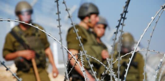 Vier israelische Soldaten stehen hinter einem Stacheldrahtzaun.