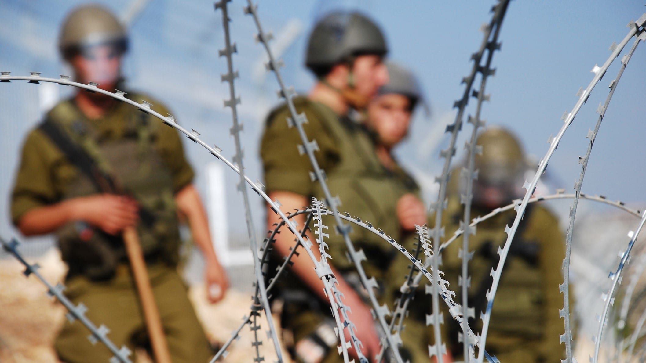 Vier israelische Soldaten stehen hinter einem Stacheldrahtzaun.