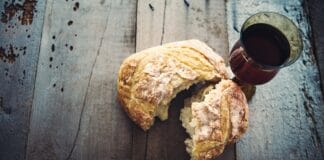 Theologe besorgt um religiöse Substanz von Gottesdiensten Ein Kelch mit Wein und ein Brotlaib stehen auf einem alten Holztisch.