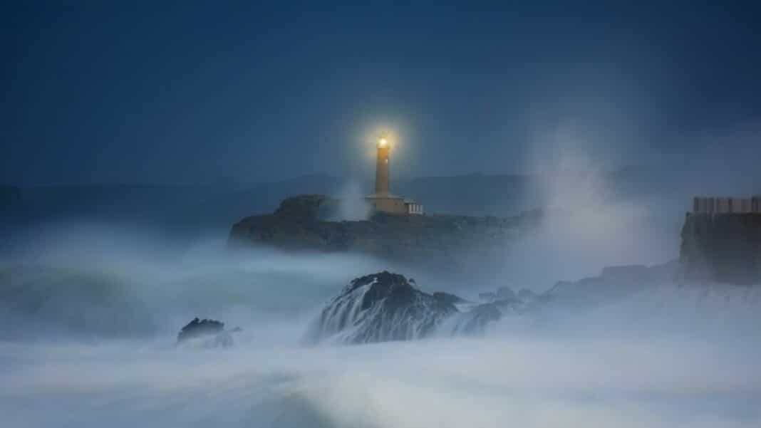 Ein Leuchtturm leuchtet nachts. Das Meer ist stürmisch.