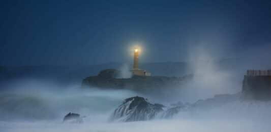 Ein Leuchtturm leuchtet nachts. Das Meer ist stürmisch.
