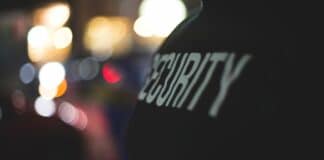 Kirche: „Du kommst hier nicht rein!“ Auf einem schwarzen T-Shirt steht in weißer Schrift "Security". Im Hintergrund sind verschwommene Lichter zu sehen.