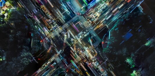 Autos fahren bei Nacht über eine beleuchtete Kreuzung.