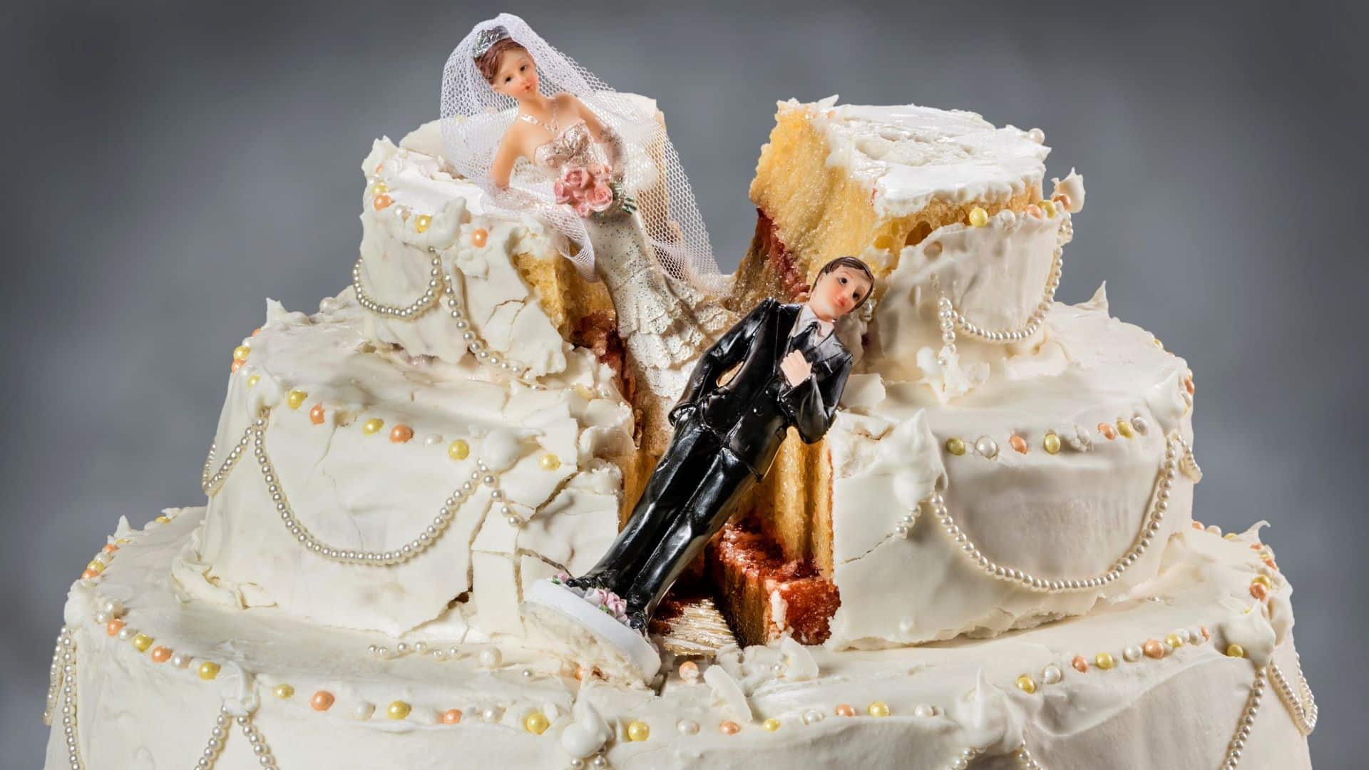 Figuren von Braut und Bräutigam liegen auf einer zerstörten Hochzeitstorte.