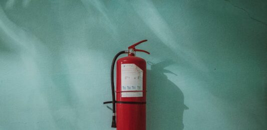 Ein roter Feuerlöscher hängt an einer türkisen Wand.