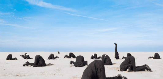 Viele Menschen im Anzug gekleidet, die ihren Kopf in einer Wüstenlandschaft in den Sand stecken