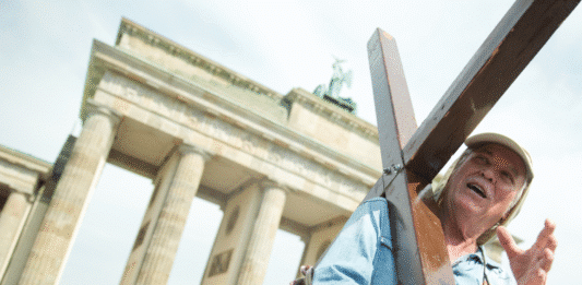 Mann mit einem Kreuz in der Hand steht vor dem Brandenburger Tor