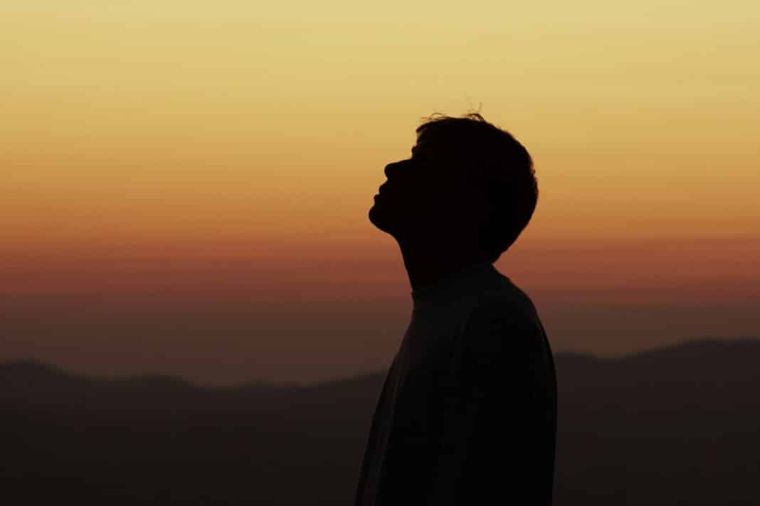 Ein Mann steht vor dem Sonnenuntergang und schaut nach oben.