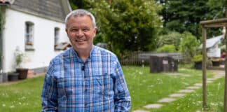 Allein, aber nicht einsam: Leben als Eremit Pater Norbert Cuypers steht vor seiner Klause neben der Kapelle "Dörnschlade" auf einer Lichtung am Waldrand in Wenden und lächelt.