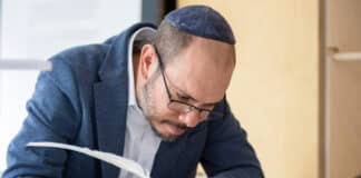 Tora-Rolle wird in Dresden öffentlich geschrieben Der Sofer Yehoshua Ze’ev Dias sitzt auf einem Stuhl und schreibt mit einer Feder die Tora-Rolle.