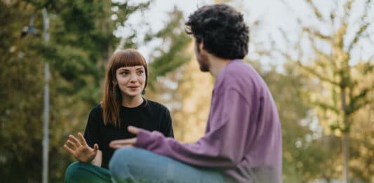 Ein Mann und eine Frau sitzen auf einer Wiese und reden.