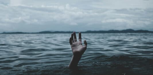 Jemand streckt seine Hand aus dem Meer. Das Wasser sieht dunkel und bedrohlich aus.