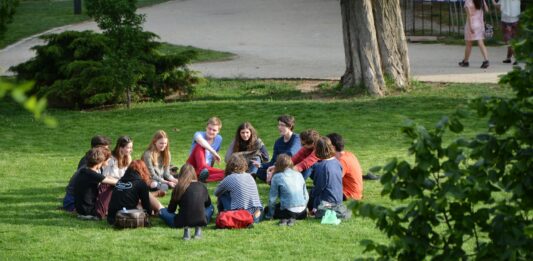 Gruppe an jungen Leuten sitzen auf einer Wiese im Kreis