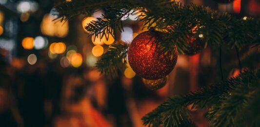 Eine rote, glitzernde Kugel hängt an einem Weihnachtsbaum.