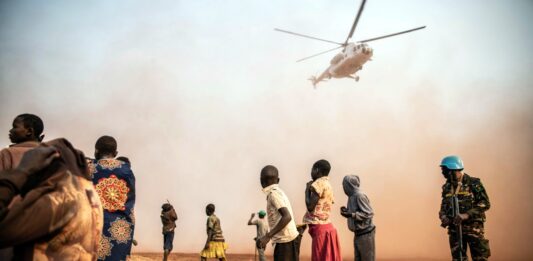 Eine Schar von Namibianern schaut auf einen Helikopter, der in der Nähe von ihnen landet und viel Staub aufwirbelt.