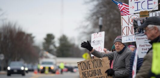 ICE Protest, ein Mann hält ein Pappschild hoch auf dem Love thy neigbor as yourself steht