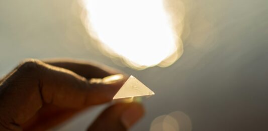 Eine Hand hält einen kleinen, dreieckigen Gegenstand, der das Licht reflektiert.