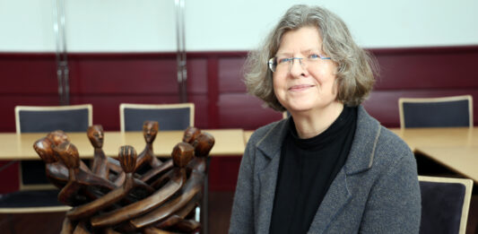 Die evangelische Pastorin Heike Jakubeit in der Zentrale der Norddeutschen Mission, neben einer Skulptur von Holzmännchen, die mit ihren Händen verbunden sind