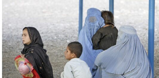 Vollverschleierte Frauen sitzen mit Kindern auf dem Boden.