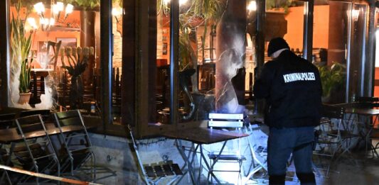 Ein Restaurant hinter einem Absperrband, das Fenster ist eingeschlagen, ein Mann von der Kriminalpolizei macht sich Notizen