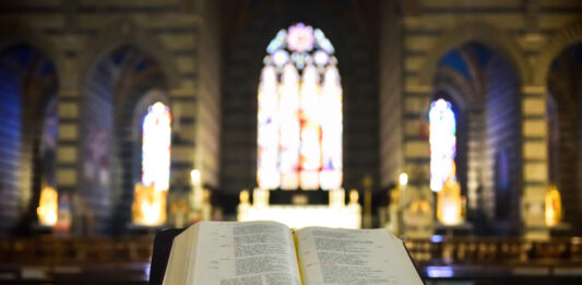 Eine aufgeschlagene Bibel vor einem bunten Kirchenfenster