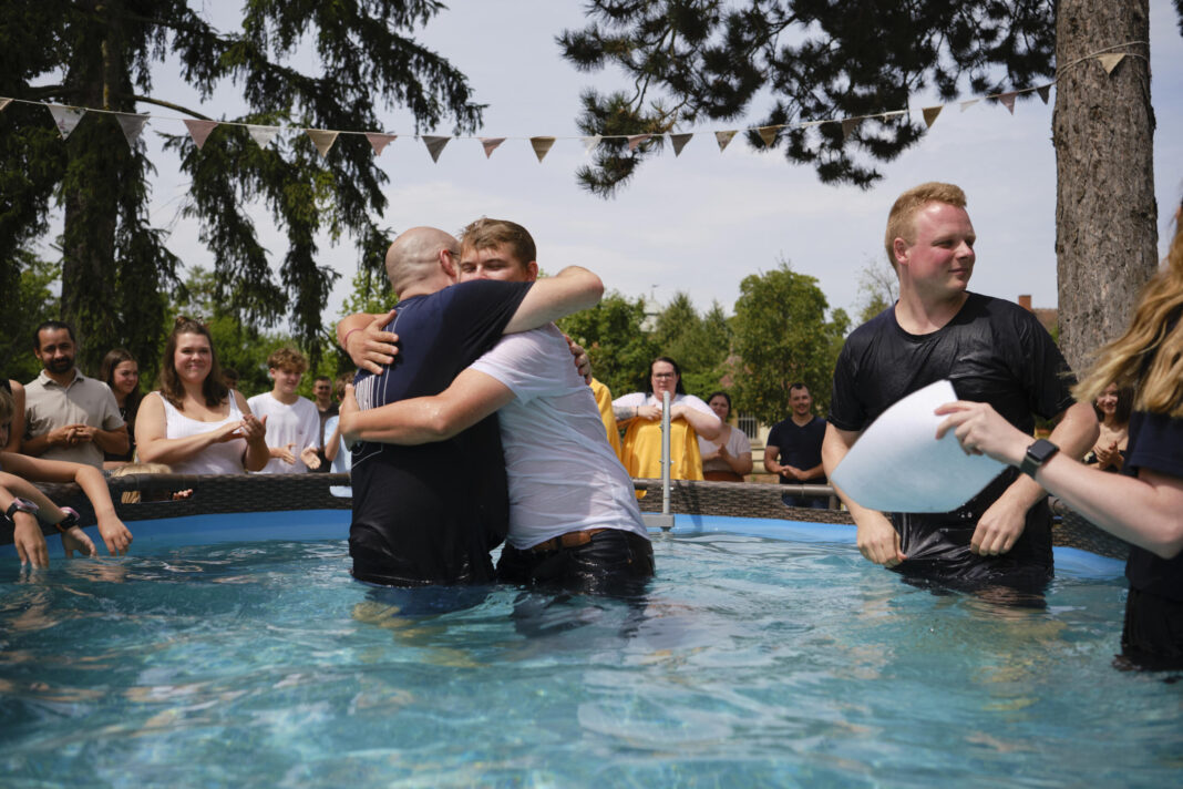 Bei einer Taufe der pulsechurch unter freiem Himmel in einem Pool umarmen sich zwei Männer.