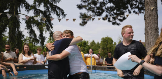 Bei einer Taufe der pulsechurch unter freiem Himmel in einem Pool umarmen sich zwei Männer.