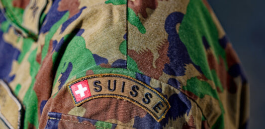 Nahaufnahme eines Schweizer Armeesoldaten mit Tarnuniform und Schweizer Flagge