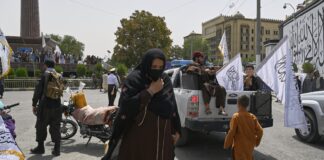 5 Jahre Taliban-Regime: Afghanistan in Not Eine Frau läuft vor wehenden Taliban Flaggen durch die Straßen.