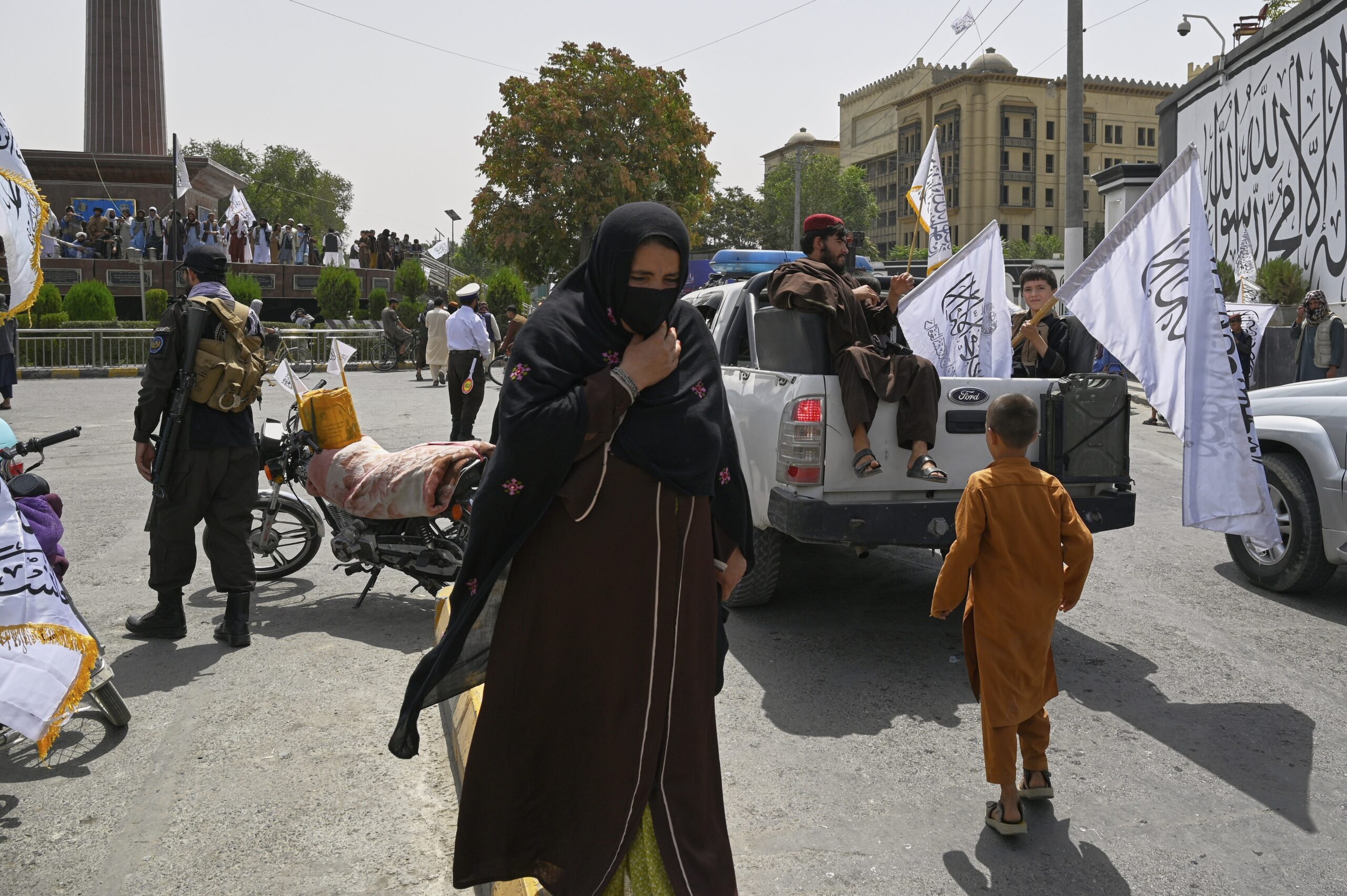Eine Frau läuft vor wehenden Taliban Flaggen durch die Straßen.