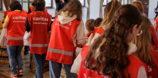 Angriffe gegen Helfer: Caritas fordert Konsequenzen Caritas Helfer mit orangenen Westen packen Taschen mit Lebensmitteln.